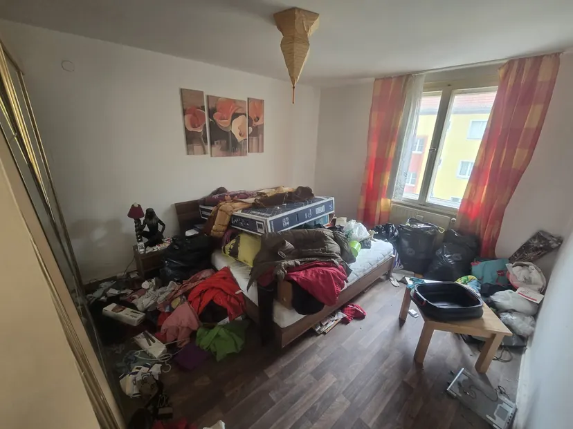 Schlafzimmer vor der Räumung: Kleidung, Taschen und Möbel bedecken Bett und Boden